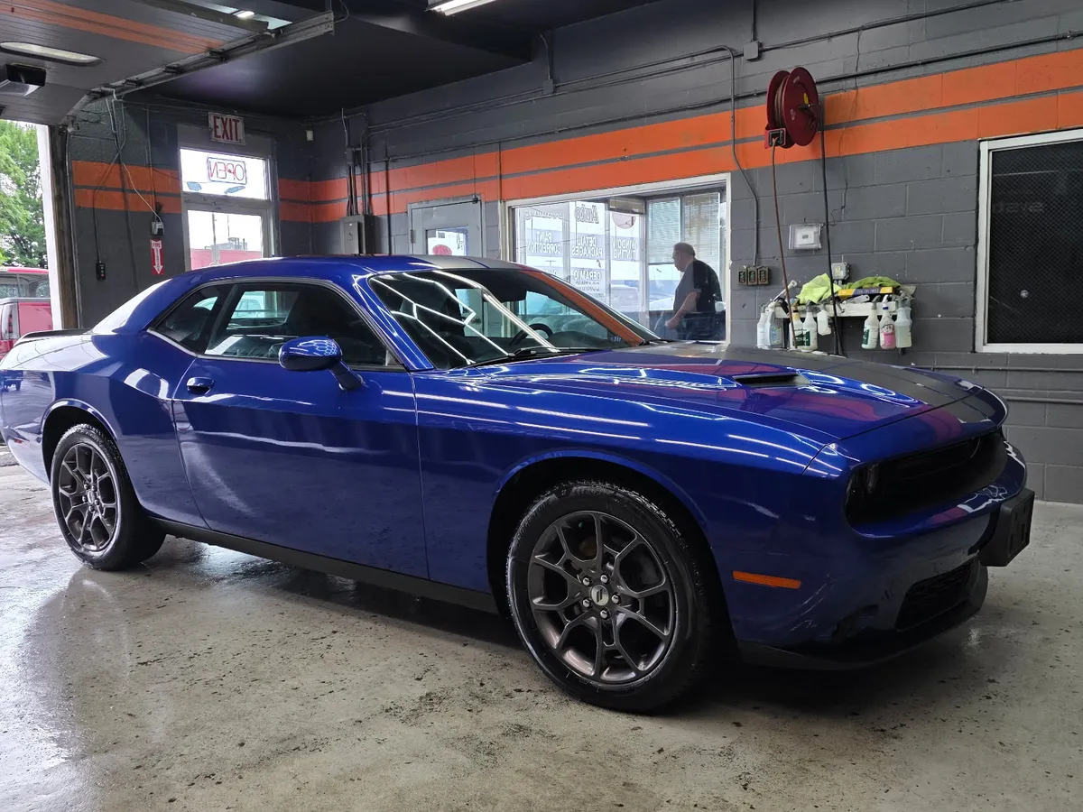 A Dodge Challenger in our bay in West Springfield, MA after a hand wash and detail — the deep, wet-look shine we hold every car to.